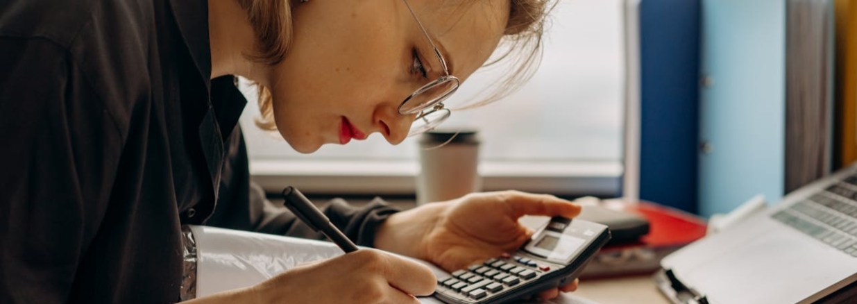 Emprendedora sacando cuentas con una calculadora mientras revisa los libros contables