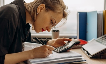 Emprendedora sacando cuentas con una calculadora mientras revisa los libros contables